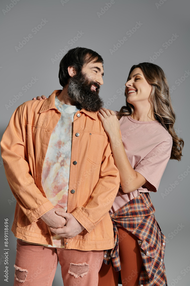 A couple in fashionable attire poses together against a grey background. A couple in fashionable attire poses together against a grey background.