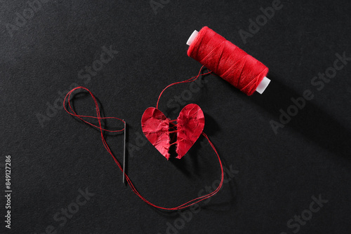 Canvas Print Halves of torn paper heart connected by thread on black background, flat lay