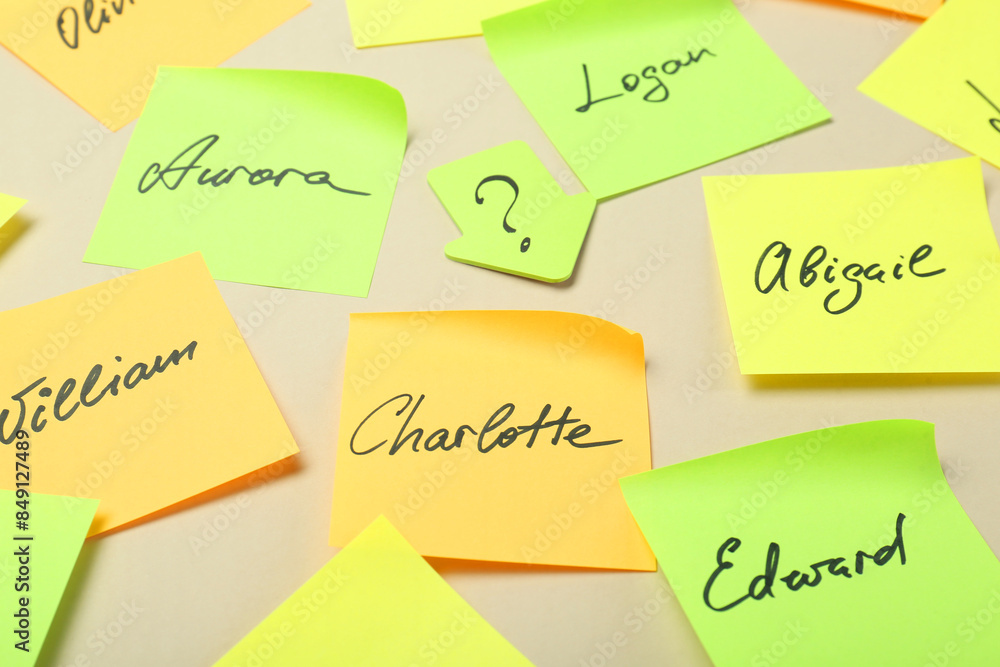 Paper stickers with different names on beige background, closeup. Choosing baby's name