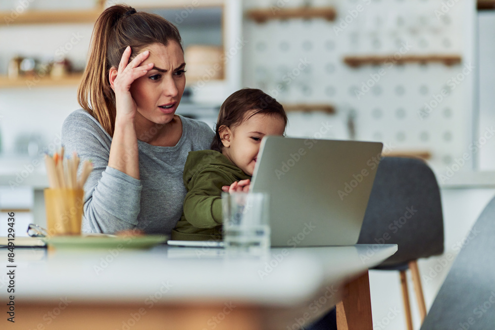A frustrated working mother reading reports on her laptop and holding her toddler A frustrated working mother reading reports on her laptop and holding her toddler