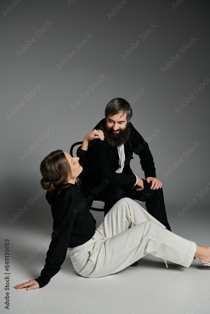 A loving couple in elegant attire poses together against a grey backdrop. A loving couple in elegant attire poses together against a grey backdrop.