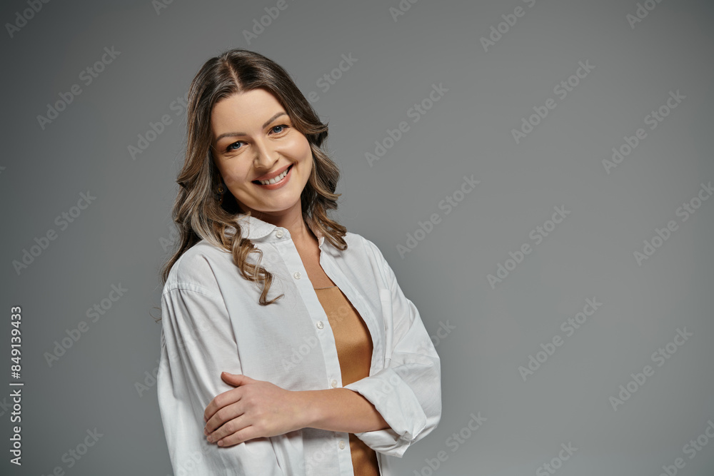 A woman in a white shirt smiles confidently while posing against a gray background. A woman in a white shirt smiles confidently while posing against a gray background.