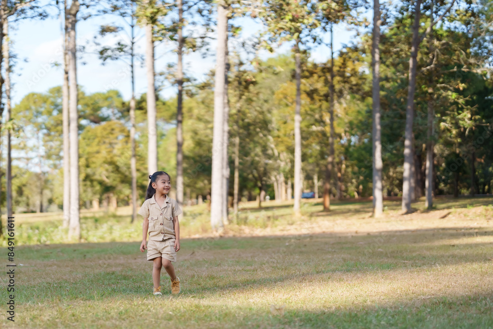 Young girl in beige outfit walking in national park, wearing blue headphones, smiling. Captures joy and energy of family vacation in nature. Bright sunny day, green trees in background. Young girl in beige outfit walking in national park, wearing blue headphones, smiling. Captures joy and energy of family vacation in nature. Bright sunny day, green trees in background.