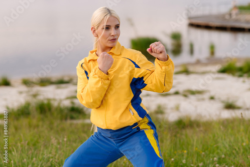 Strong woman karate fighter standing in fighting stance outdoors in park