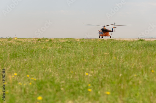 Orange helicopter on a green meadow preparing to take off. No people. Sunny summer day. Transport helicopter for aerial forest protection. Foreground blur.