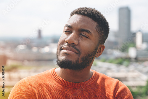 Man With Beard Relaxing In Orange Sweater In Urban Setting On Sunny Day