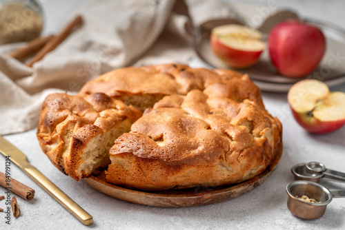 Traditional apple pie on a wooden plate on a light culinary background. Charlotte pie on a platter in closeup. Delicious homemade cakes on the kitchen table