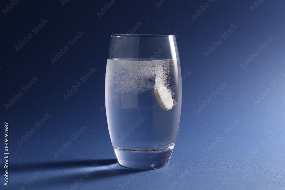 Effervescent pill dissolving in glass of water on blue background Effervescent pill dissolving in glass of water on blue background