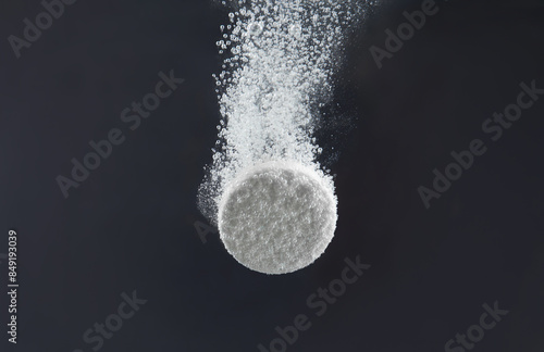 Effervescent pill dissolving in water on dark background, closeup photo