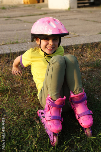 A small and cheerful girl in a pink helmet and roller skates is sitting on the stairs