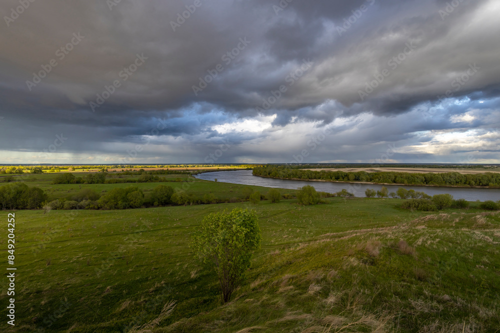 The horizon is visible in the distance, featuring a river. The lighting is dramatic, with the sun breaking through the clouds, creating a contrast of light and shadow across the landscape. The horizon is visible in the distance, featuring a river. The lighting is dramatic, with the sun breaking through the clouds, creating a contrast of light and shadow across the landscape.