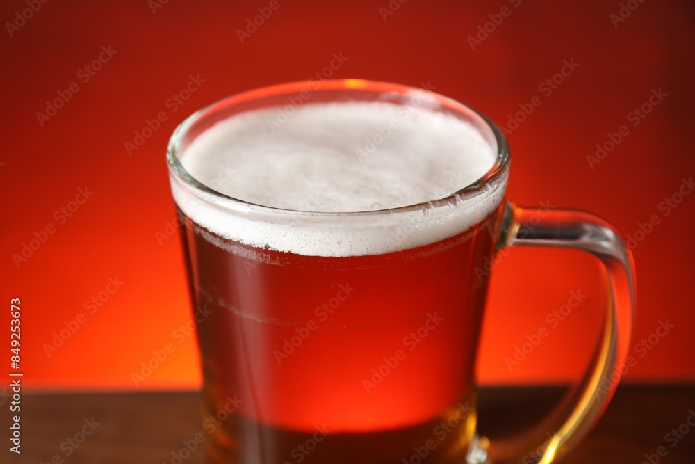 Mug with fresh beer on table against red background, closeup Mug with fresh beer on table against red background, closeup