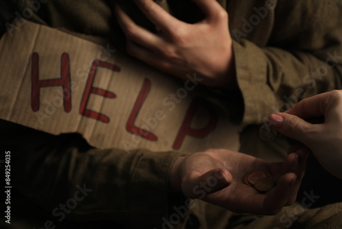 Woman giving coins to homeless with help sign, closeup. Charity and donation