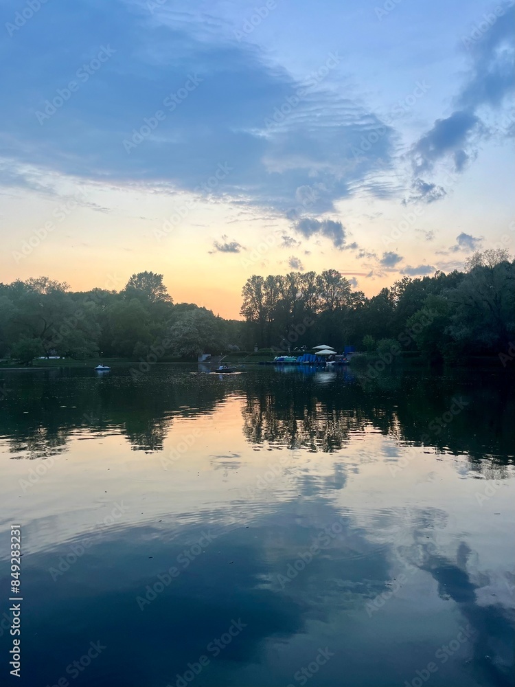 Fototapeta premium Fantastic cloudy sky reflection on the lake surface, trees silhouettes reflection on the lake, evening twilights lake in the park