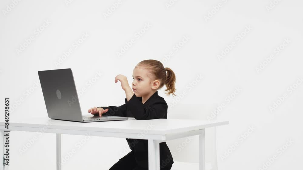 A cute little girl in front of a laptop experiences emotions from an idea or solution to a problem, the girl uses a computer for distance learning on a light studio background.