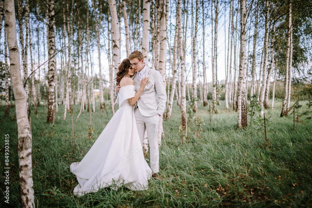Valmiera, Latvia - September 9, 2023 - A bride and groom stand lovingly embraced in a serene birch forest, with tall trees and lush green grass surrounding them on their wedding day. Valmiera, Latvia - September 9, 2023 - A bride and groom stand lovingly embraced in a serene birch forest, with tall trees and lush green grass surrounding them on their wedding day.
