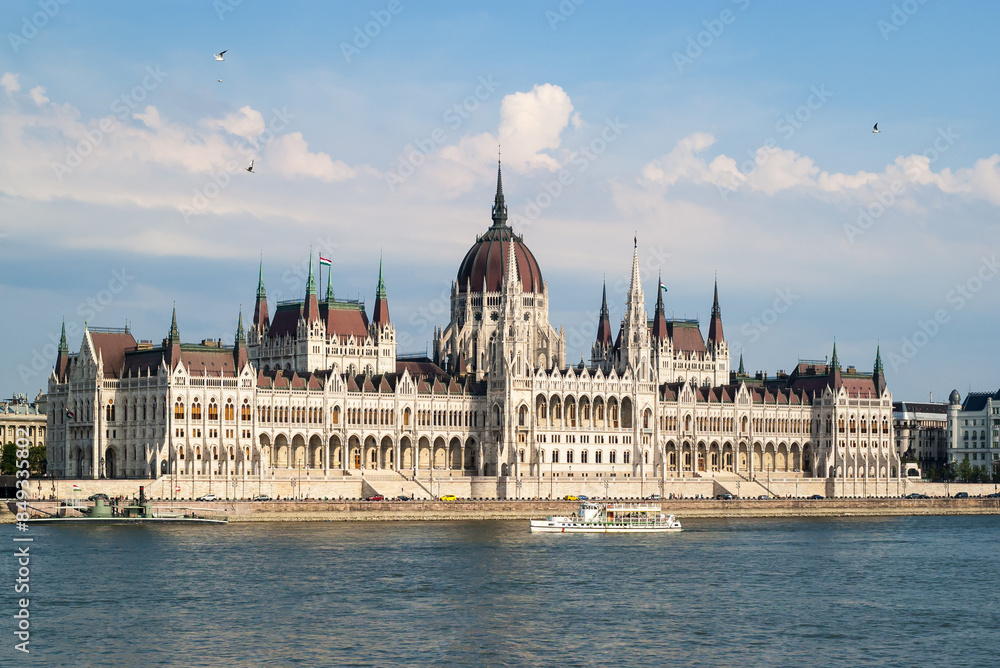 Obraz premium Hungarian parliament building, tourist boat along the Danube river and flying birds in the sky, Budapest, Hungary.
