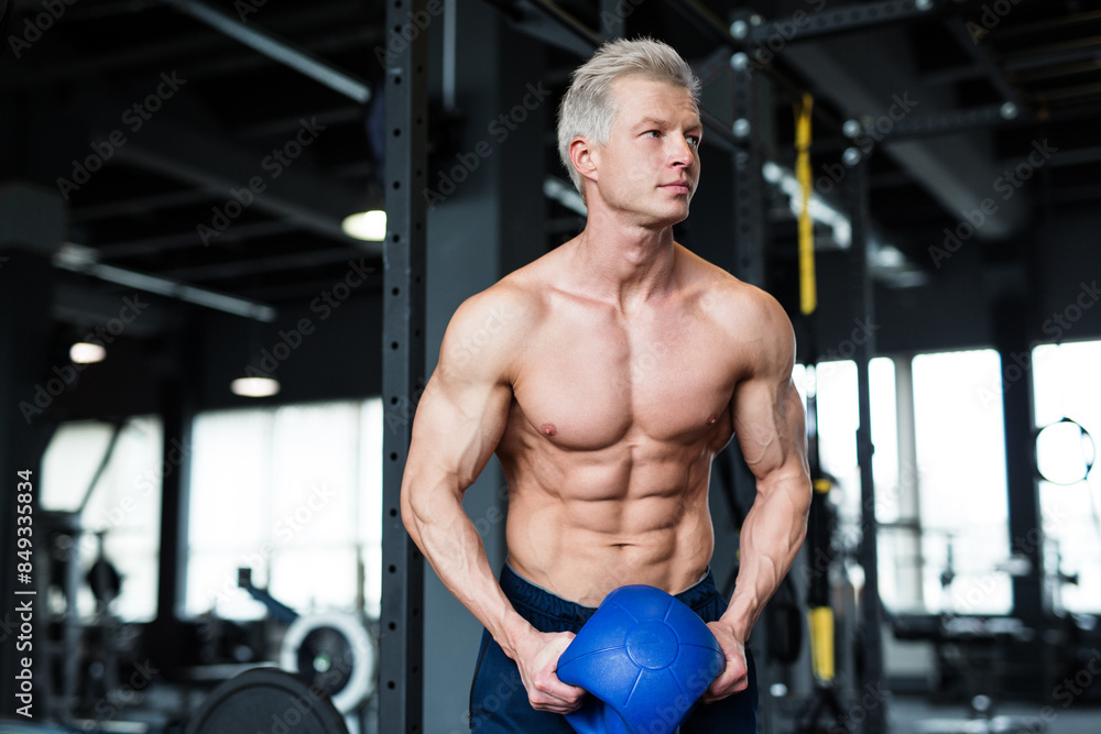 Naklejka premium Muscular man exercising with a kettlebell, showing dedication and focus on fitness goal at the gym