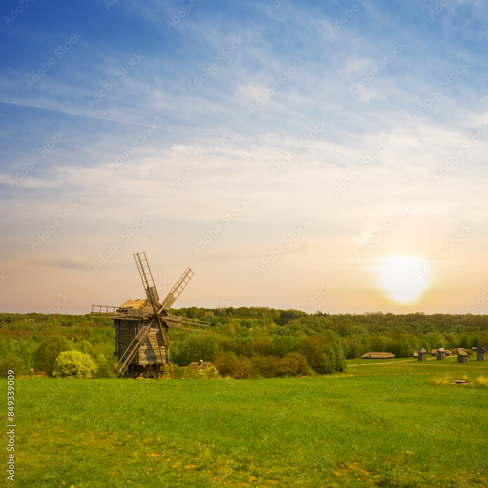 Naklejka premium old wooden medieval windmill among green rural fields at the sunset
