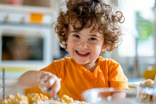 Joyful curly-haired child wearing orange shirt baking cookies