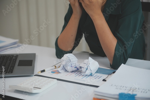 Asian women sitting in a home office With stress and eye strain.Tired businesswoman holding eyeglasses and massaging nose bridge. There are tablets, laptops, and coffee. photo
