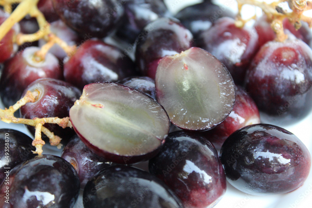 Fototapeta premium Halved dark purple or black grape with stem, seedless grape fruit, on white background