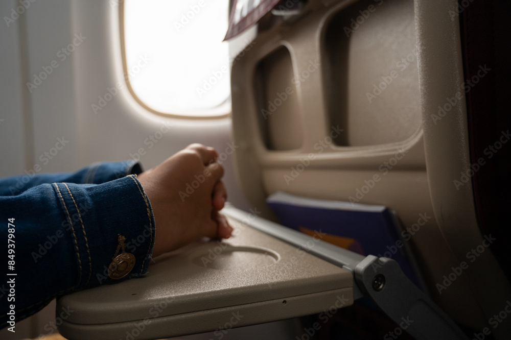 A person is praying in an airplane. The person is wearing a blue jacket A person is praying in an airplane. The person is wearing a blue jacket