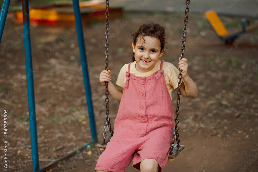 Smiling kid girl playing on a swing outdoor on a playground. Children summer activity. Smiling kid girl playing on a swing outdoor on a playground. Children summer activity.