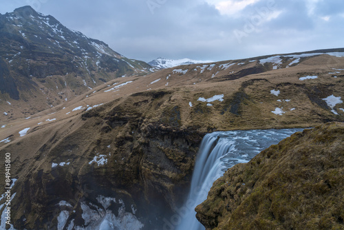 Skógafoss waterfall with an astounding width of 25 meters and a drop of 60 meters seen from the top of the cliff with snow covered mountains in the background, South coast, Iceland