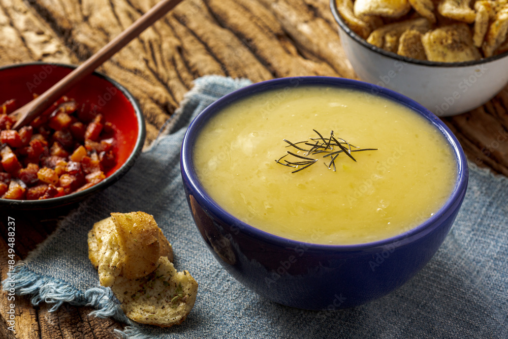 Delicious cassava cream (Caldo ou Creme de Mandioca) or cassava soup, typical of Brazilian cuisine, served in a blue porcelain bowl, on top of a typical rustic farm table, top view with selective focu Delicious cassava cream (Caldo ou Creme de Mandioca) or cassava soup, typical of Brazilian cuisine, served in a blue porcelain bowl, on top of a typical rustic farm table, top view with selective focu