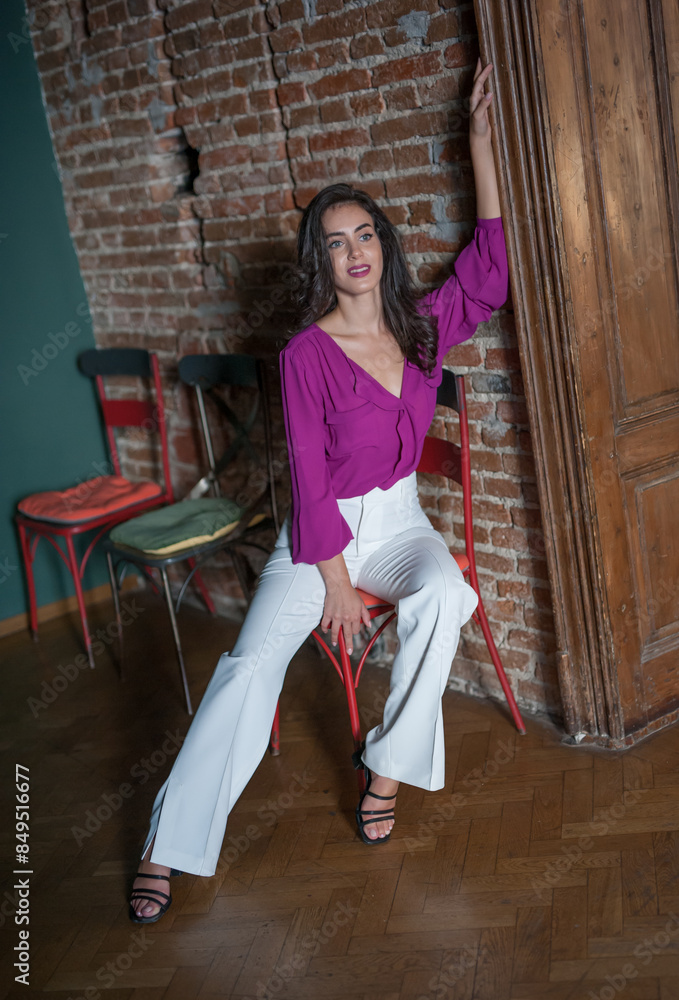 Beautiful young brunette woman in a purple blouse and white pants posing outdoor. Portrait of a beautiful young brunette woman with long hair posing fashion