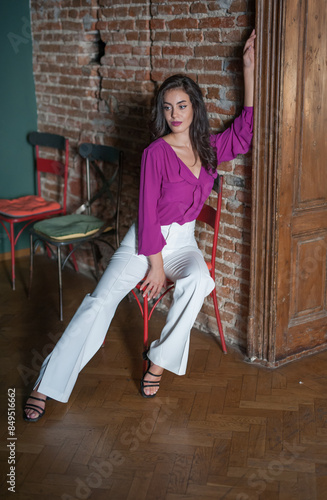 Obraz na płótnie Beautiful young brunette woman in a purple blouse and white pants posing outdoor. Portrait of a beautiful young brunette woman with long hair posing fashion w salonie
