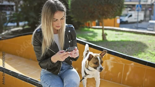 Blonde woman using smartphone on park bench next to her attentive dog. photo