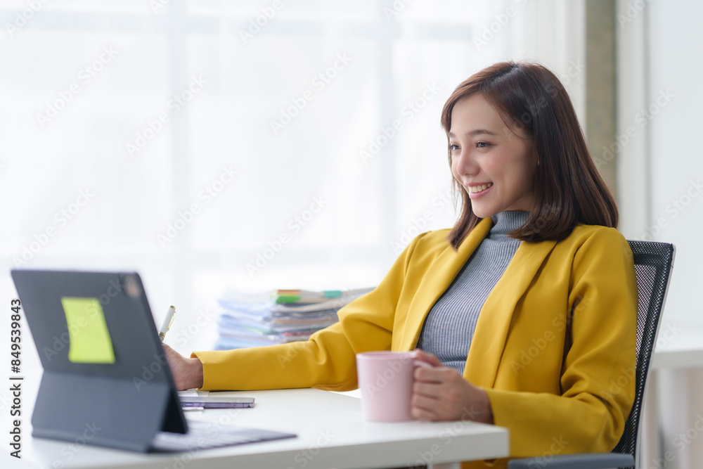 Businesswoman smiling while working on a laptop at her desk with a cup in hand. Remote work, productivity, and technology concept. Businesswoman smiling while working on a laptop at her desk with a cup in hand. Remote work, productivity, and technology concept.