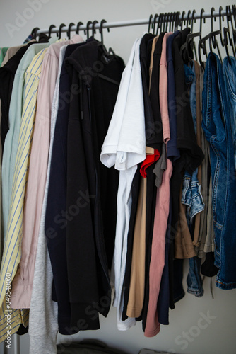 Casual clothes like shirts, sweaters, and jeans hang on a rack in a home closet. 