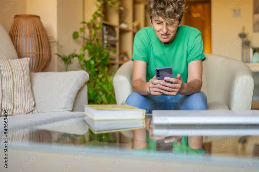 Smiling Mature Woman Enjoying Her Free Time With A Smartphone At Home. Concept Of Online Banking, Online Shopping, Social Media, Checking Emails Or Messages. Natural Light Smiling Mature Woman Enjoying Her Free Time With A Smartphone At Home. Concept Of Online Banking, Online Shopping, Social Media, Checking Emails Or Messages. Natural Light