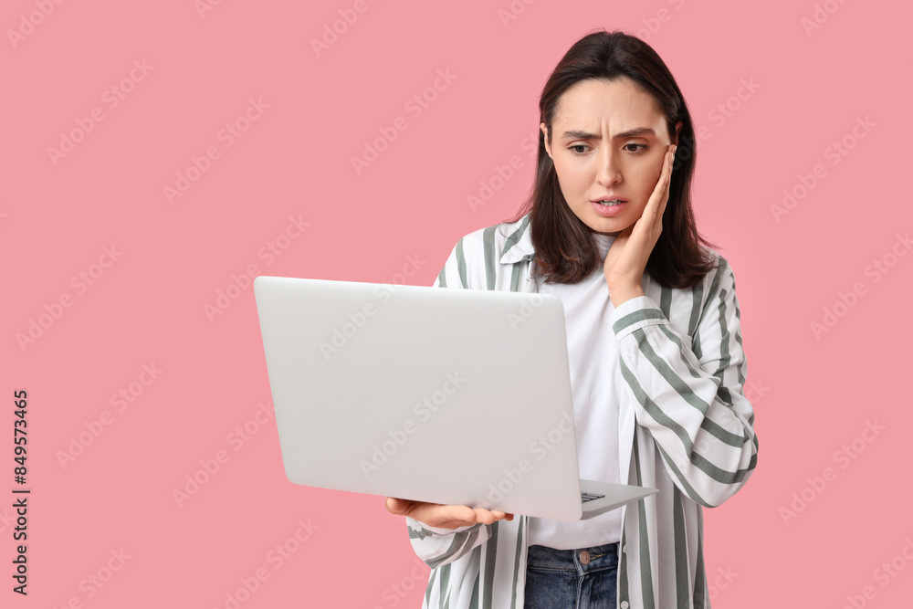 Confused young woman with laptop on pink background Confused young woman with laptop on pink background