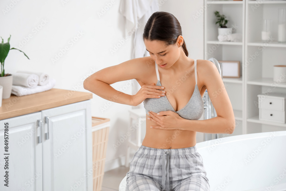 Young woman checking her breast in bathroom. Cancer awareness concept Young woman checking her breast in bathroom. Cancer awareness concept