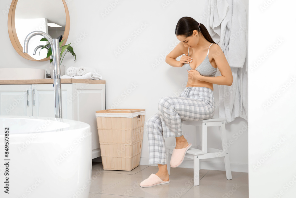 Young woman checking her breast on stool in bathroom. Cancer awareness concept Young woman checking her breast on stool in bathroom. Cancer awareness concept