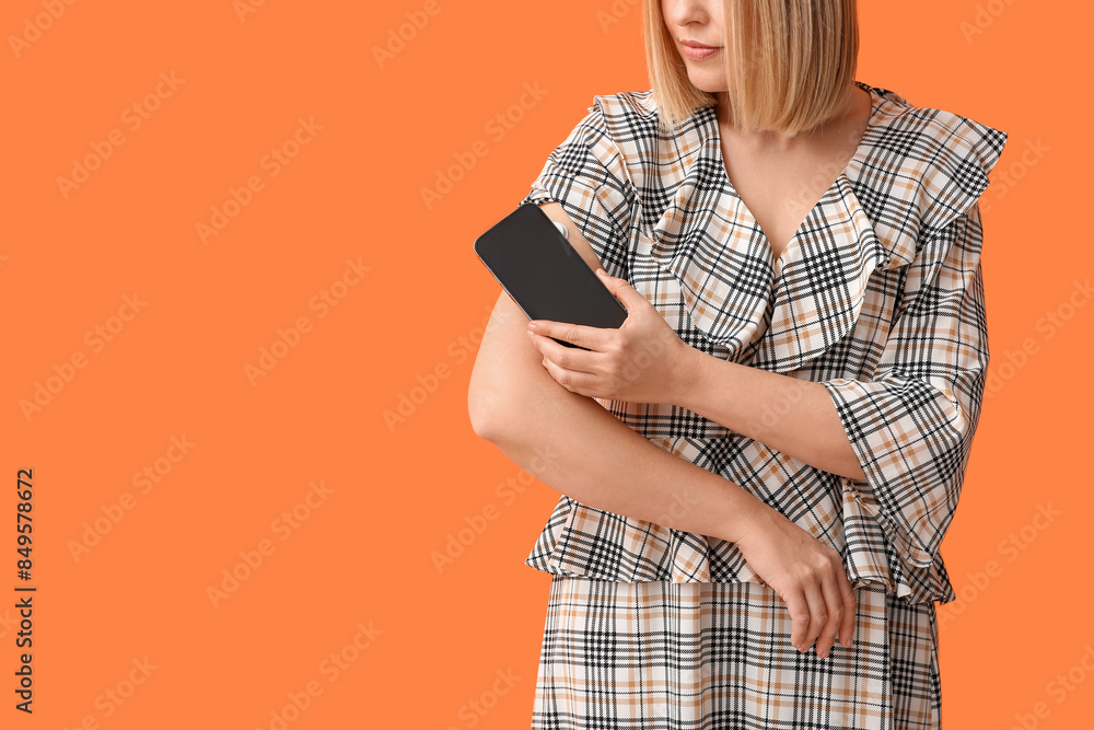 Woman with glucose sensor for measuring blood sugar level and phone on orange background. Diabetes concept