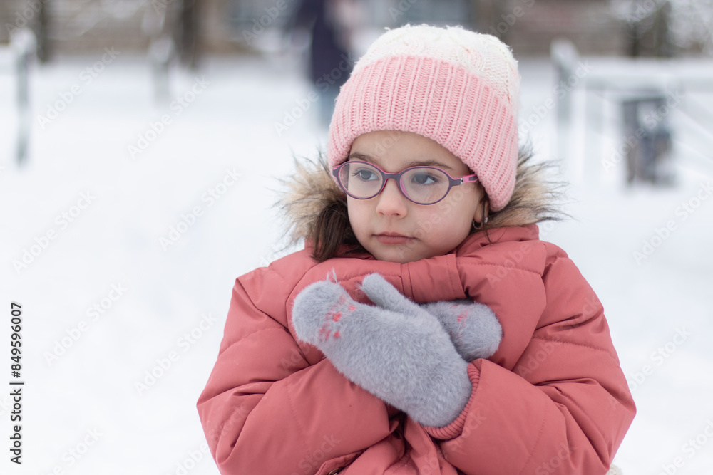 Little beautiful girl in a knitted hat, glasses and warm clothes outdoors in winter. Children's games in the snow Little beautiful girl in a knitted hat, glasses and warm clothes outdoors in winter. Children's games in the snow