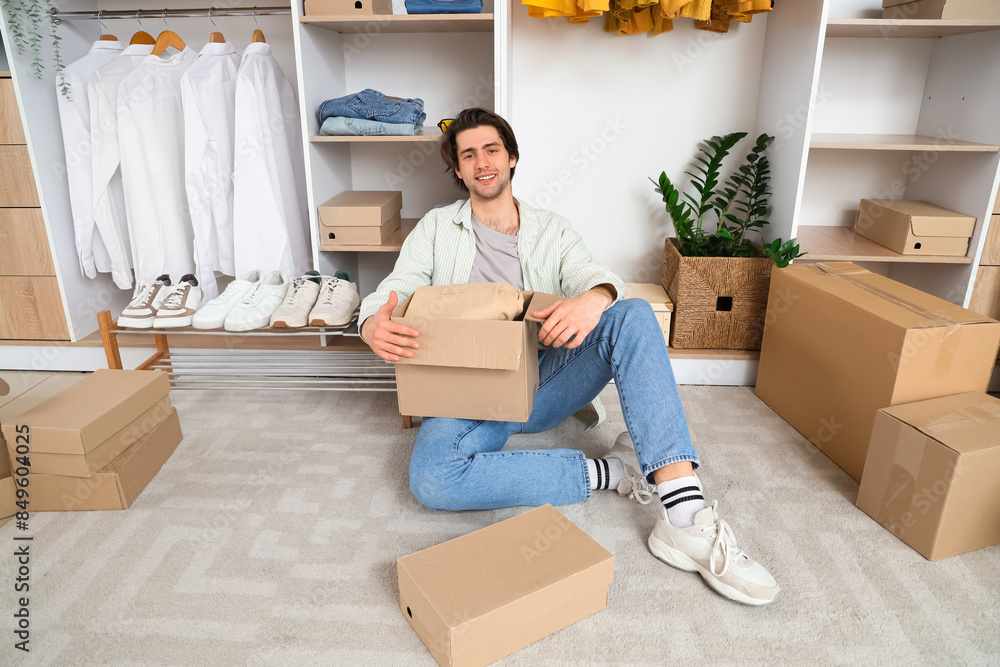 Handsome young happy man with wardrobe boxes and stylish clothes sitting in dressing room Handsome young happy man with wardrobe boxes and stylish clothes sitting in dressing room