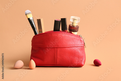 Red cosmetic bag with lipsticks, perfume bottle and makeup accessories on beige background