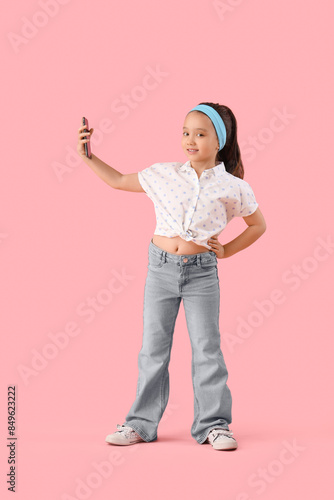 Portrait of fashionable little girl taking selfie on pink background
