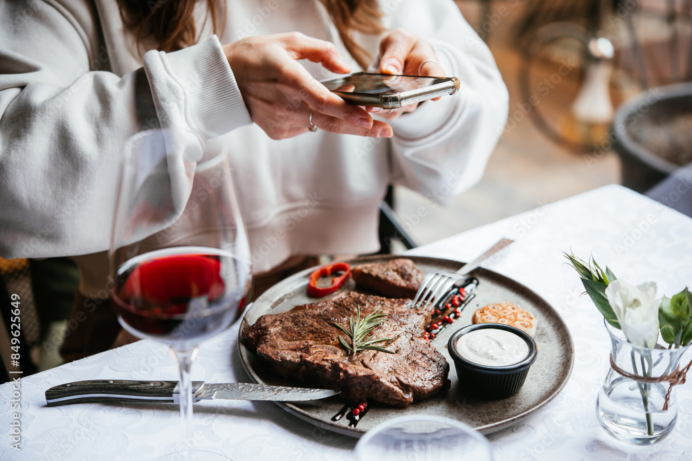 Taking a photo of beef steak served with red wine for dinner at a restaurant.