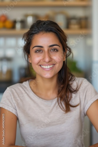 Smiling beautiful middle eastern young woman sitting at her home kitchen looking at the camera 