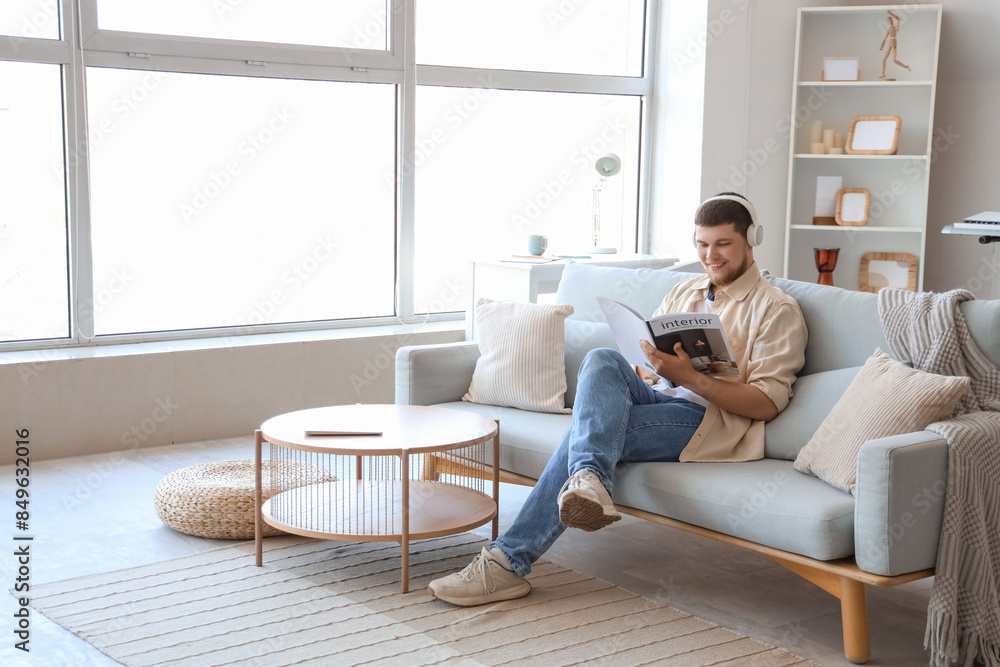 Young bearded man in headphones reading magazine on sofa at home Young bearded man in headphones reading magazine on sofa at home
