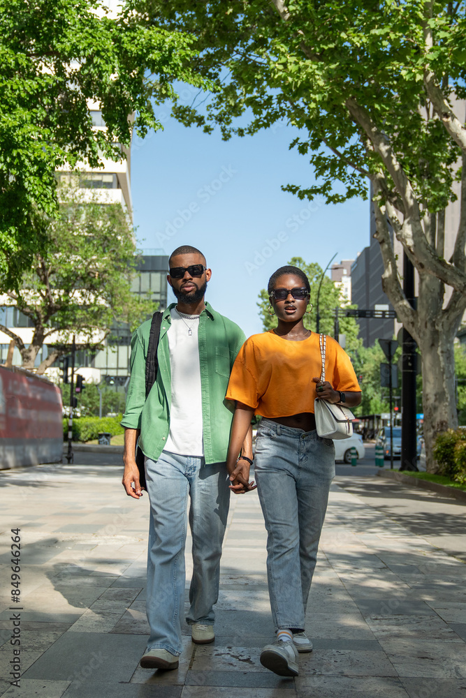 Romantic African American couple holding hands while walking down street in summer time. Serious self-confident black man and stylish girl going along road, students spend free time together strolling