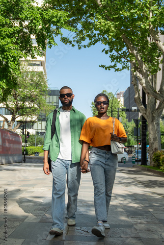 Romantic African American couple holding hands while walking down street in summer time. Serious self-confident black man and stylish girl going along road, students spend free time together strolling © DimaBerlin