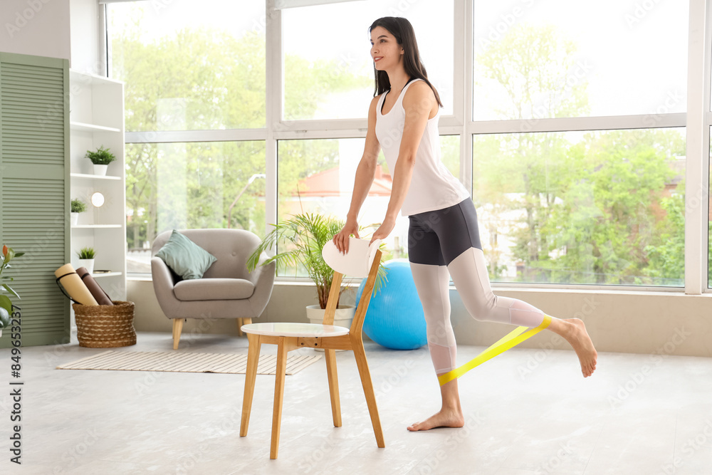 Sporty young woman with elastic band and chair training at home Sporty young woman with elastic band and chair training at home